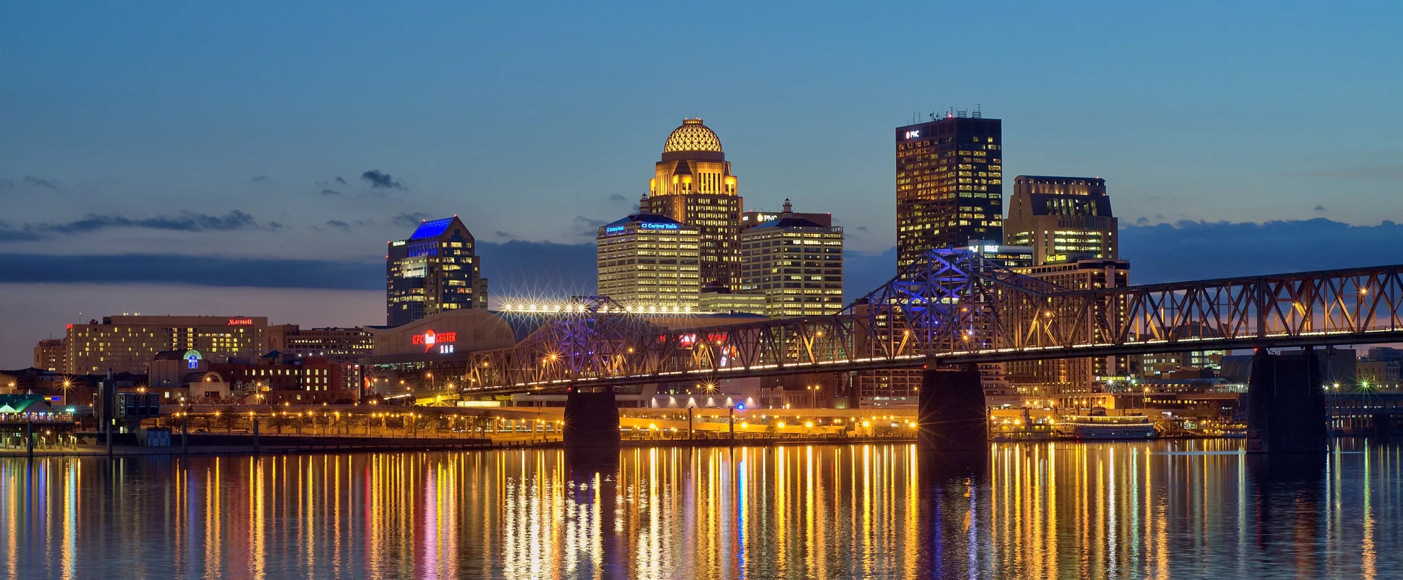 Dusk skyline photo of the Louisville waterfront with light reflections in the Ohio River