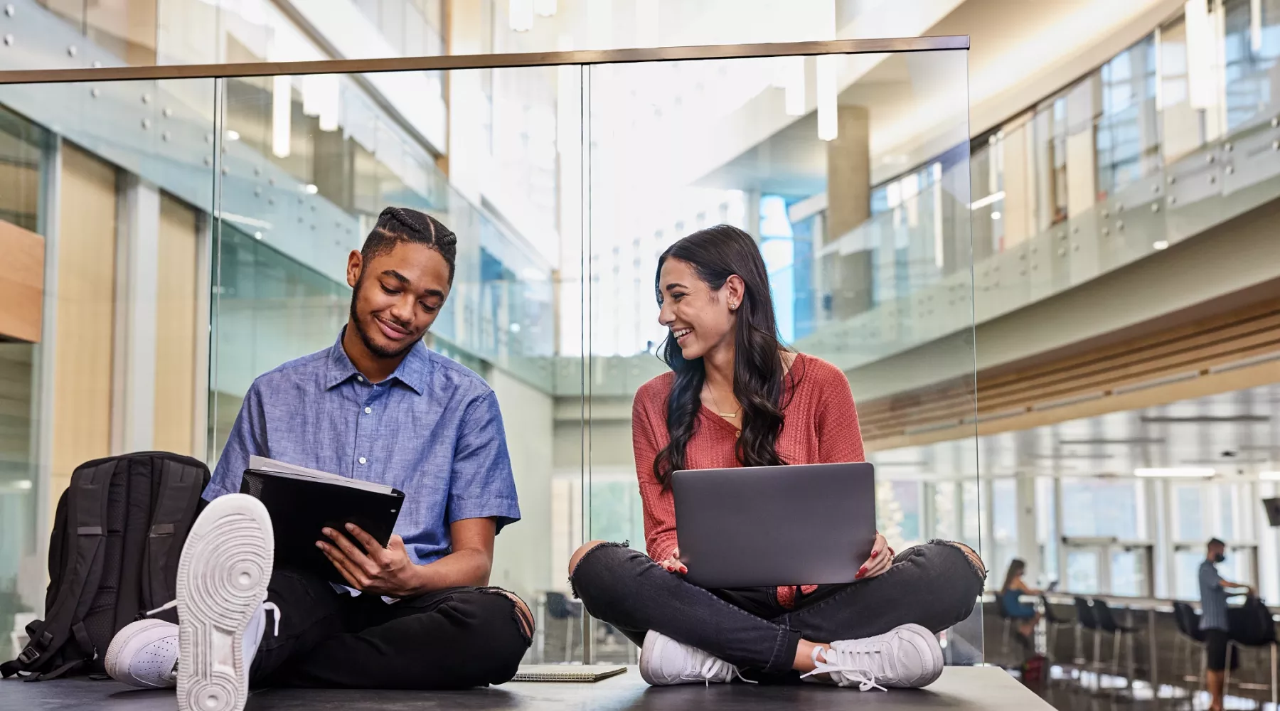 Two students are sitting on the floor while they study and do academic research on the second floor of the Belknap Academic Building.