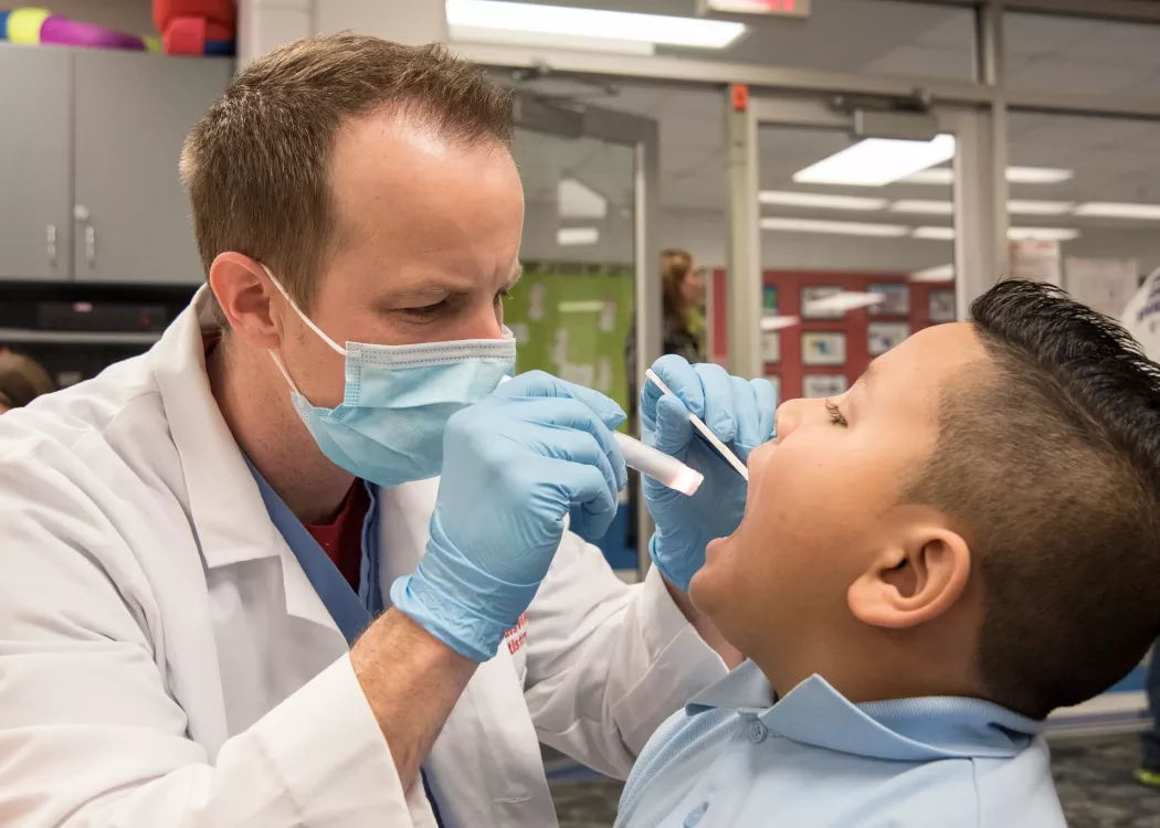 Dental student looks into an elementary student's mouth on Give Kids a Smile Day.