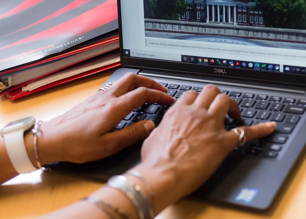 Employee typing on laptop in a UofL office