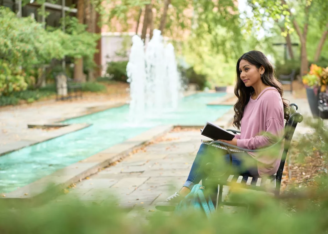 Student takes a pause from reading at the fountain area and looks up.