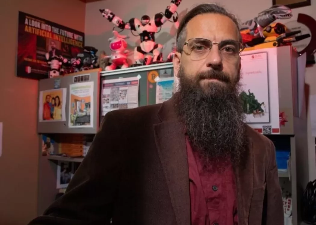 Roman Yampolskiy posing in his office, which is filled with toy robots and posters related to AI.