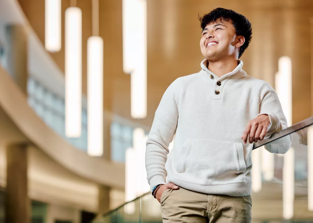 A smiling young male student standing on a modern indoor balcony