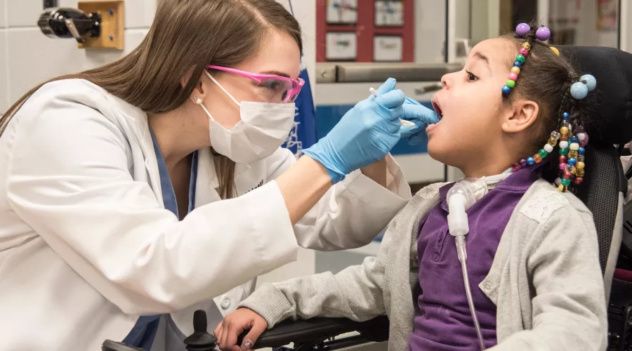 Elementary student opens her mouth for a dental student to give her an exam.