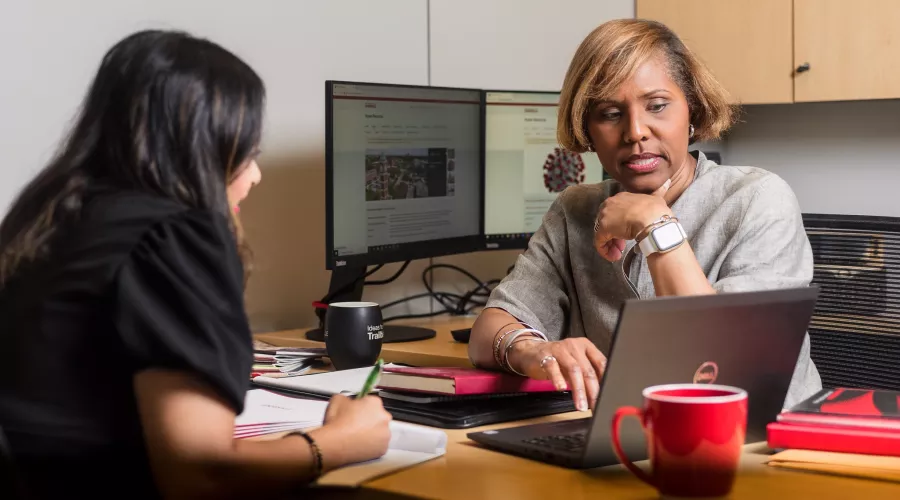Two female employees seated during a meeting discussing content on screen of laptop