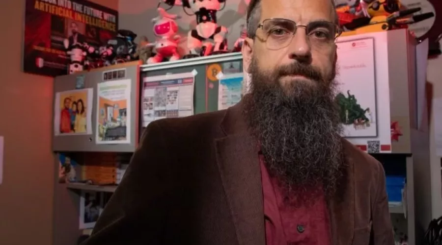 Roman Yampolskiy posing in his office, which is filled with toy robots and posters related to AI.