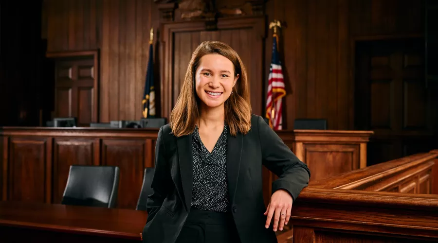 A young woman in a business suit stands in a mock courtroom