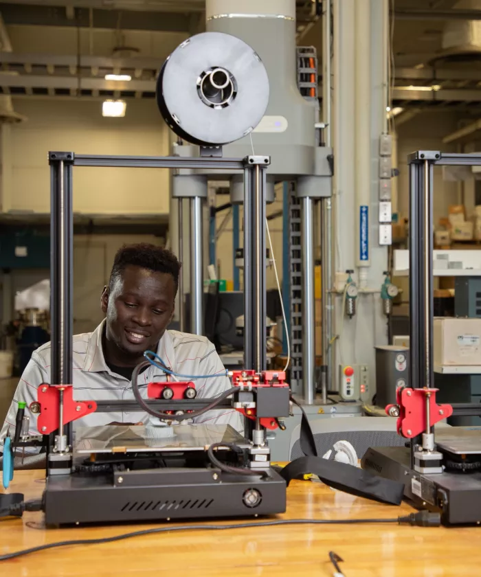 An engineering student looking down at a 3d printer in the AMIST lab.